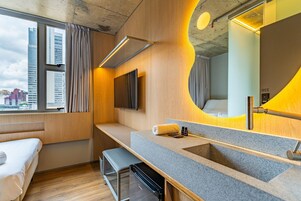 Una habitación de hotel moderna con un ventanal grande, un lavamanos integrado, una banca y un televisor de pantalla plana.