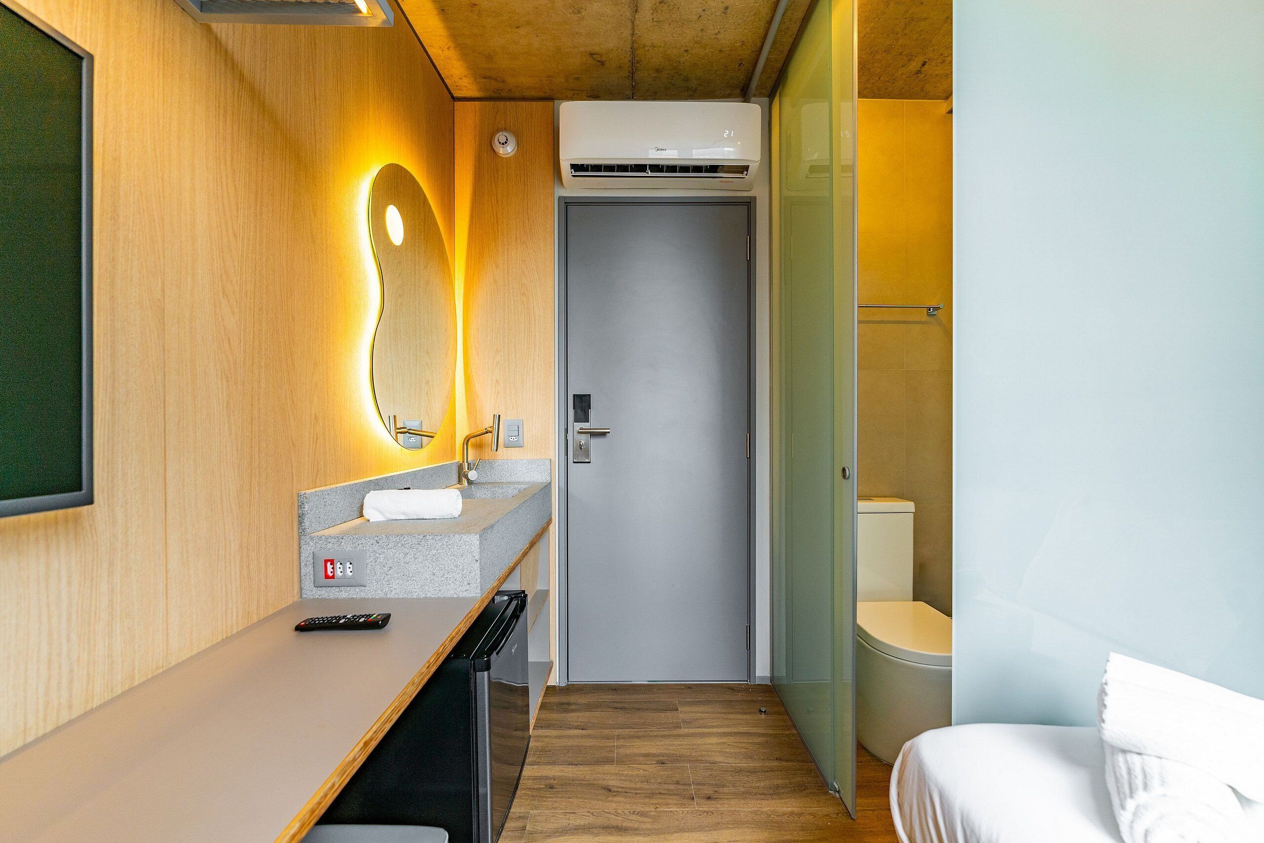 A compact hotel room with a wooden wall, a small sink, a toilet, and a bed.