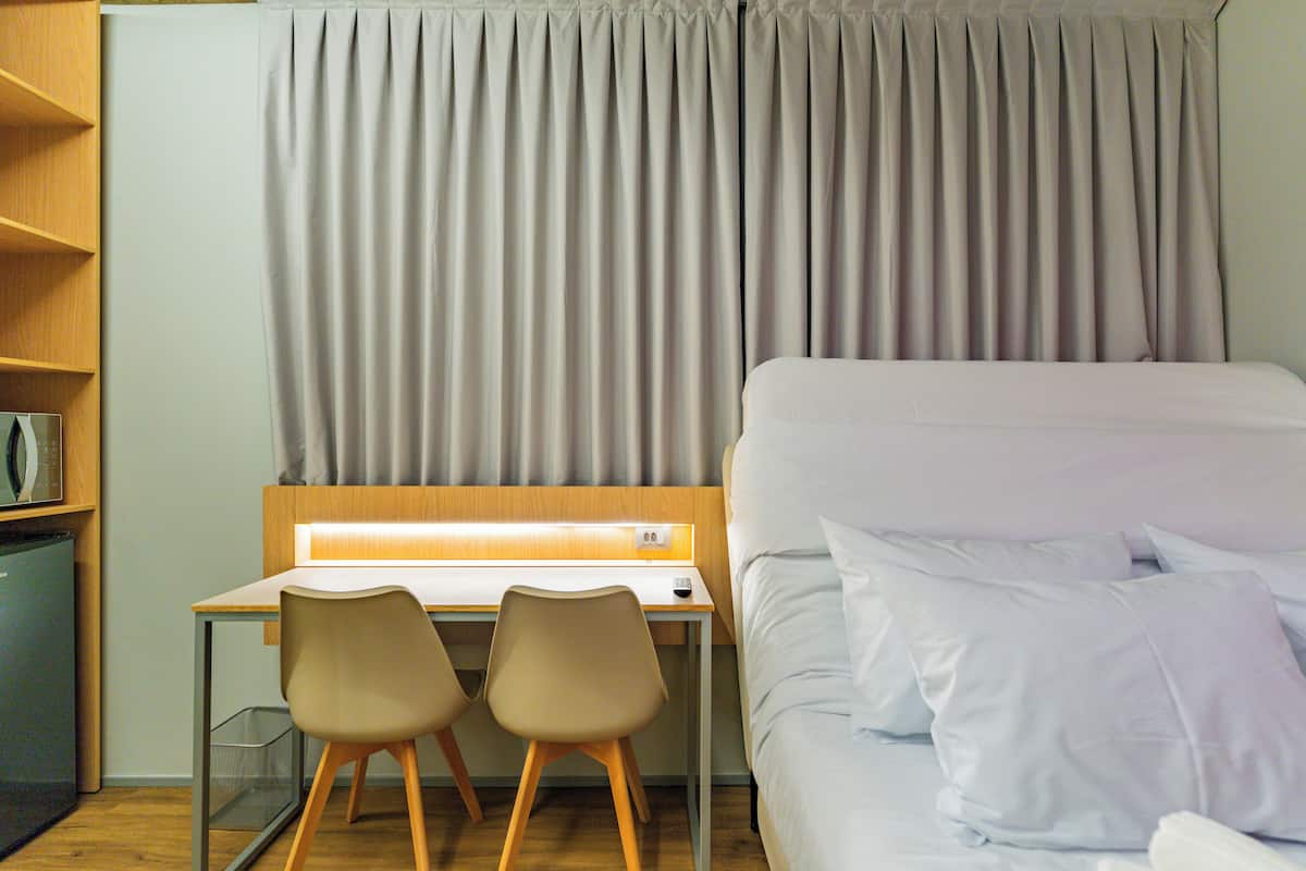 A hotel room with a bed, two chairs, a desk, and a curtain.