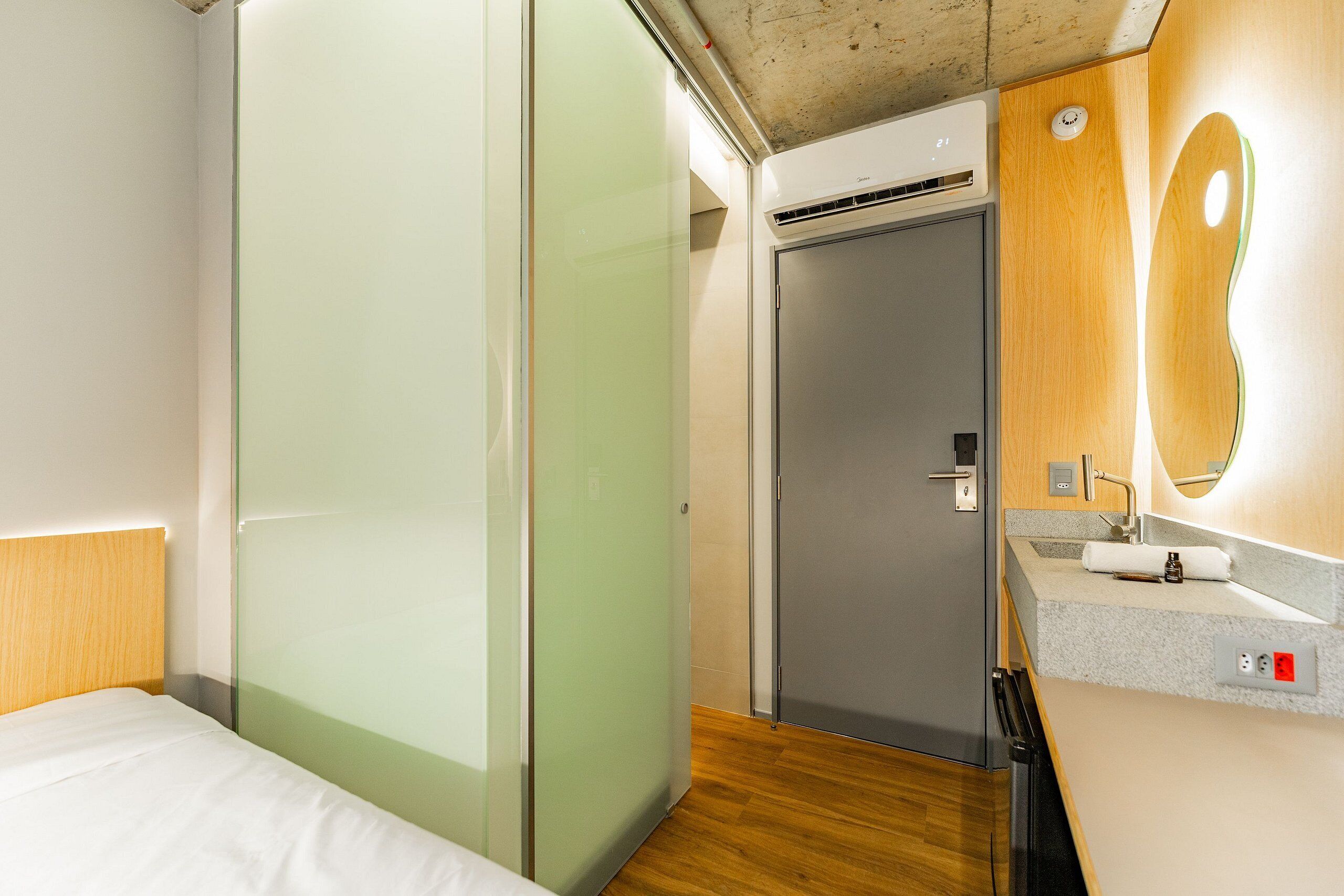 Habitación de hotel con cama, armario, baño con lavabo y espejo, y ducha.