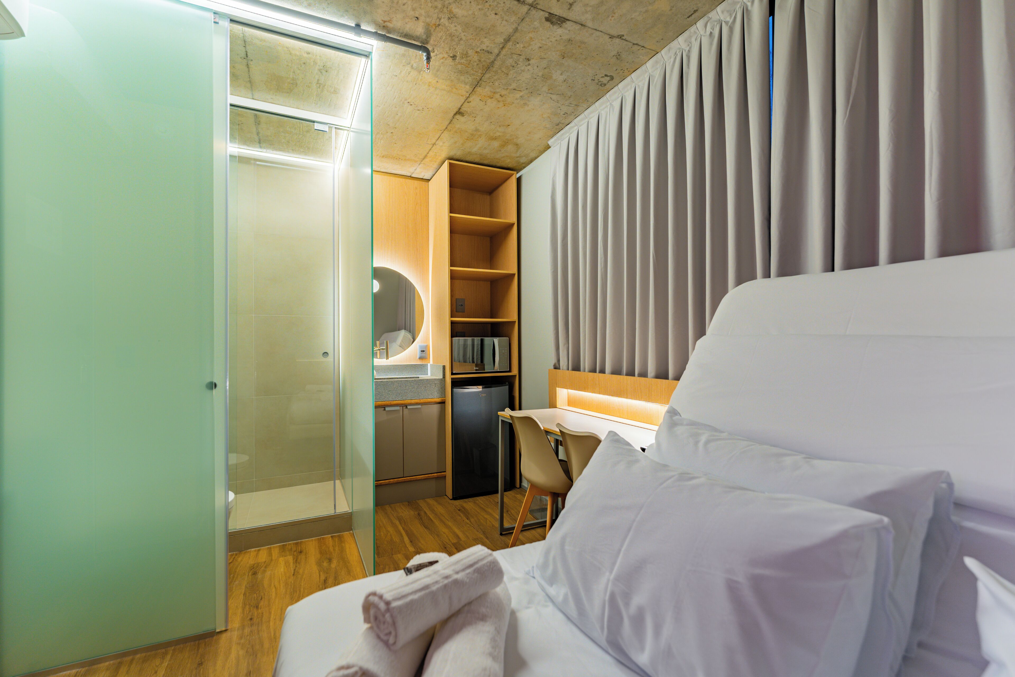 A hotel room with a bed, a desk, a chair, a wardrobe, and a small kitchenette.