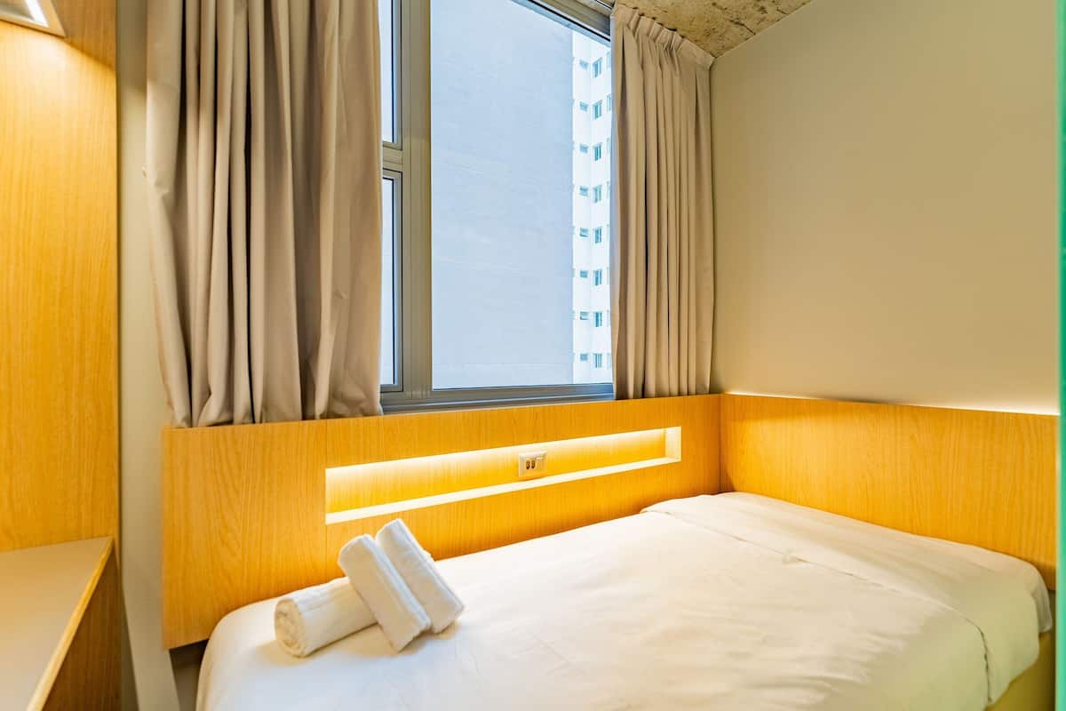 A hotel room with a bed, curtains, a window, and a headboard with built-in lighting.