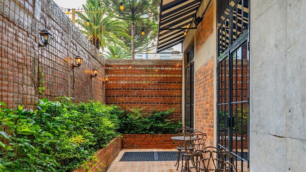 A brick-walled courtyard with a tiled floor, metal furniture, and a view of a building through a window. - Linked Batel by Xtay (Curitiba)