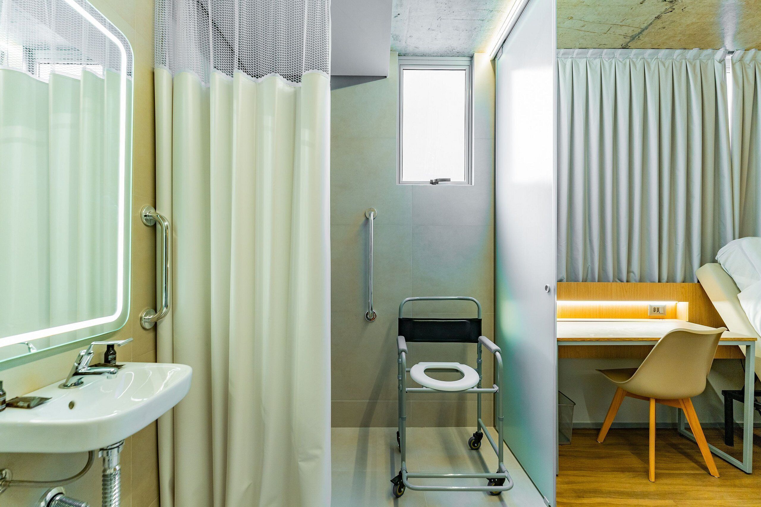 A bathroom with a sink, a toilet on a mobile stand, a shower curtain, and a window.