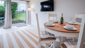 Un comedor con una mesa redonda de madera, sillas blancas y un televisor montado en la pared.