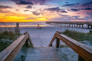 A wooden boardwalk leading to a pier extending into the water, with a lifeguard stand visible on the beach. - Jacksonville Beach Oasis with Sparkling Private Pool (Jacksonville Beach)