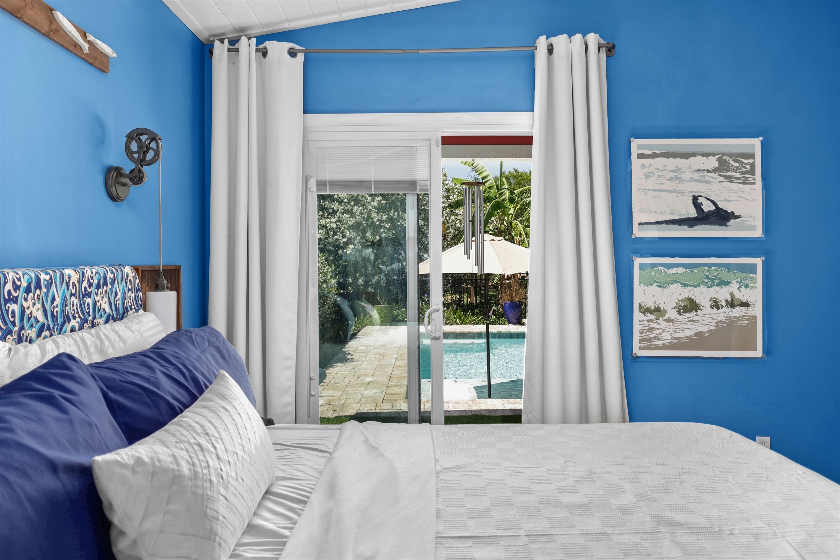 A bedroom with a bed, a view of a swimming pool, and two framed pictures on the wall.