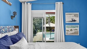 Quarto com uma cama, vista para uma piscina e duas imagens emolduradas na parede.