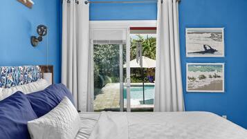 A bedroom with a bed, a view of a swimming pool, and two framed pictures on the wall.