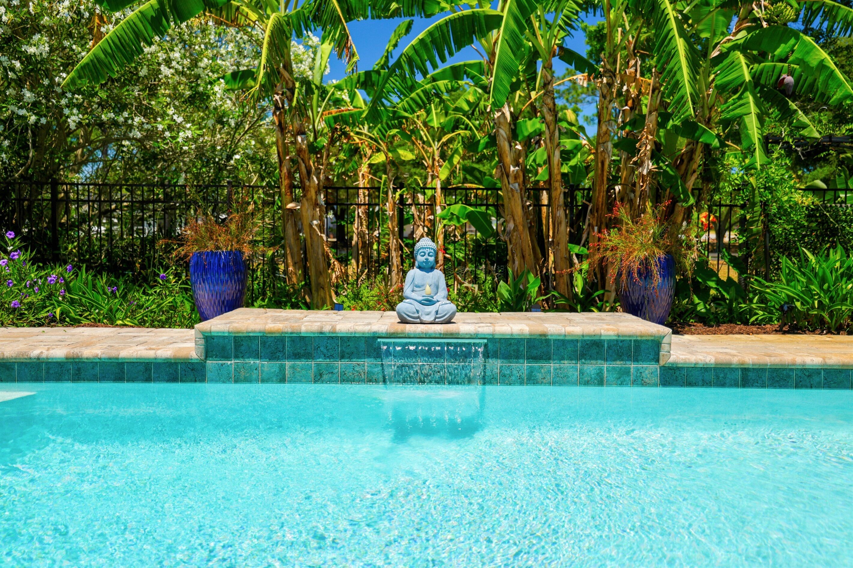 A meditative statue by a pool with tropical foliage in the background.