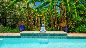 Estátua serena à beira de uma piscina, com vegetação tropical ao fundo.