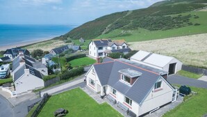 Zona residencial costera con casas, una playa y colinas al fondo.