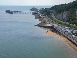 Una zona costera con un muelle que se adentra en el mar, un faro y una carretera que serpentea a lo largo de la costa.