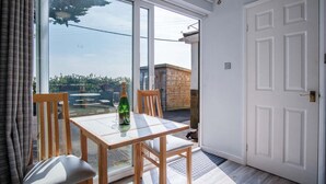 A room with a glass door leading to a balcony, a wooden table with chairs, and a bottle of champagne.