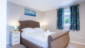 A neatly made bed with a headboard, a bedside table with a lamp, and a window with curtains.