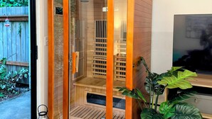 A sauna with a wooden exterior and glass doors, located in a room with a TV and potted plants. - Cedar Heights w sauna/bonfire (Lynnwood)