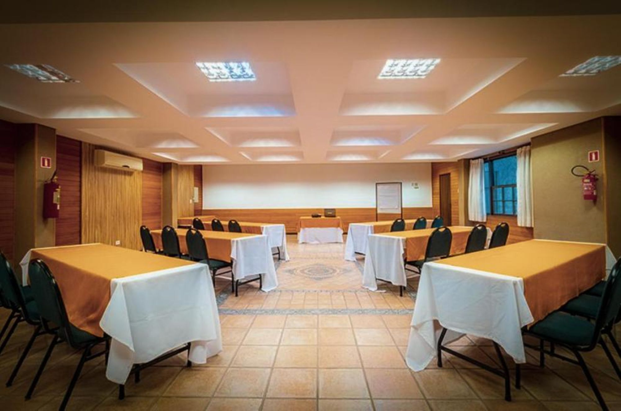 A conference room with multiple tables and chairs, equipped with a projector screen and a whiteboard.