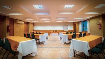 A conference room with multiple tables and chairs, equipped with a projector screen and a whiteboard.