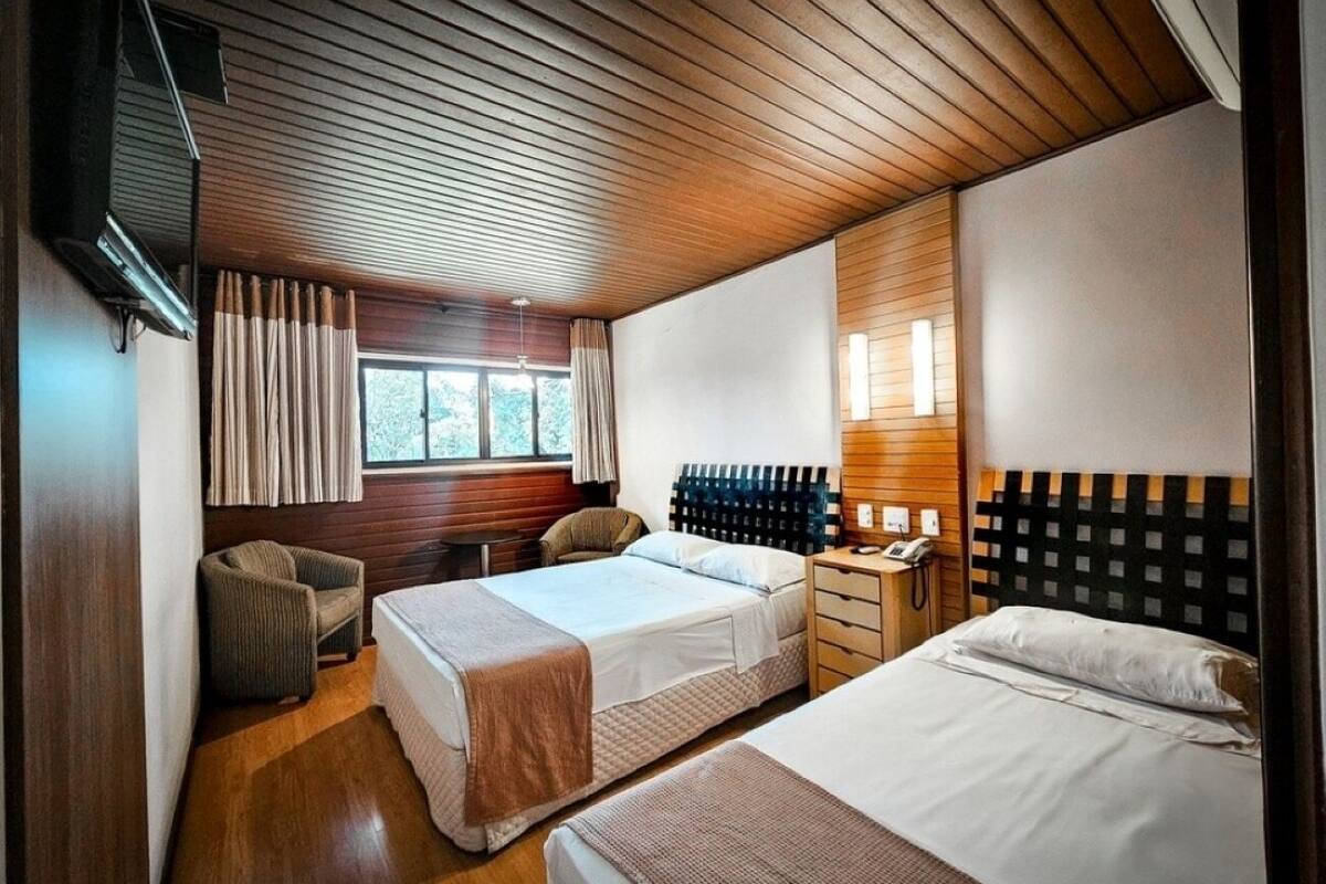 Habitació d'hotel moderna amb dos llits, sòl de fusta, una finestra gran amb cortines, una petita zona de seients i un telèfon fixat a la paret.