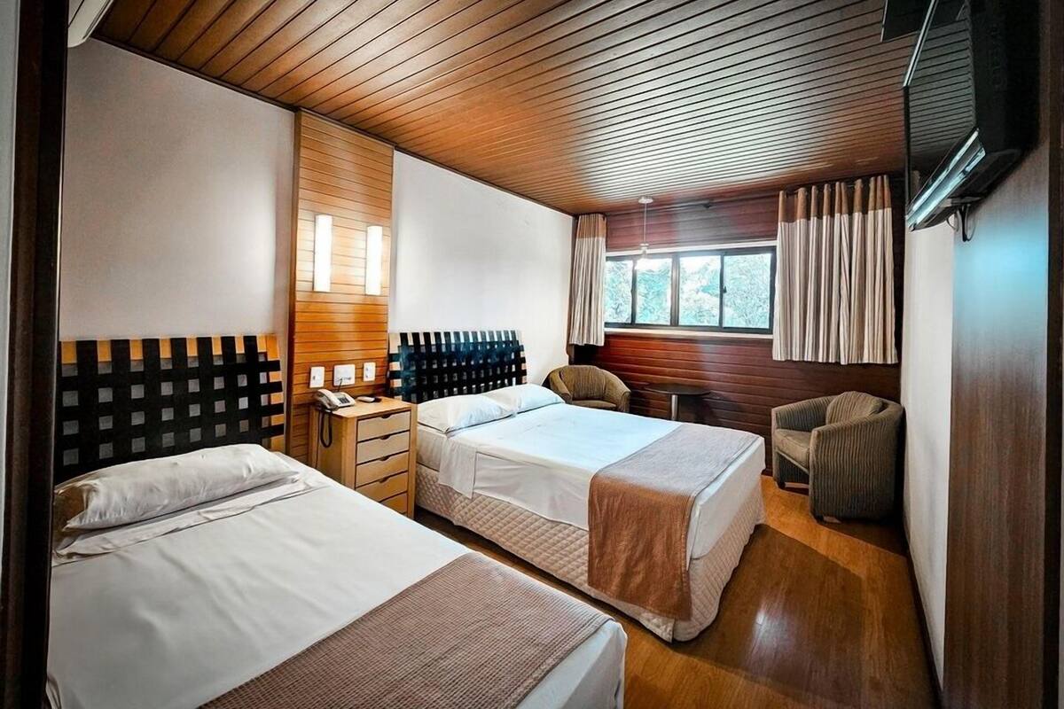 Habitació d'hotel amb dues lliteres, sostre de fusta, televisió, finestra amb cortines i taula petita.