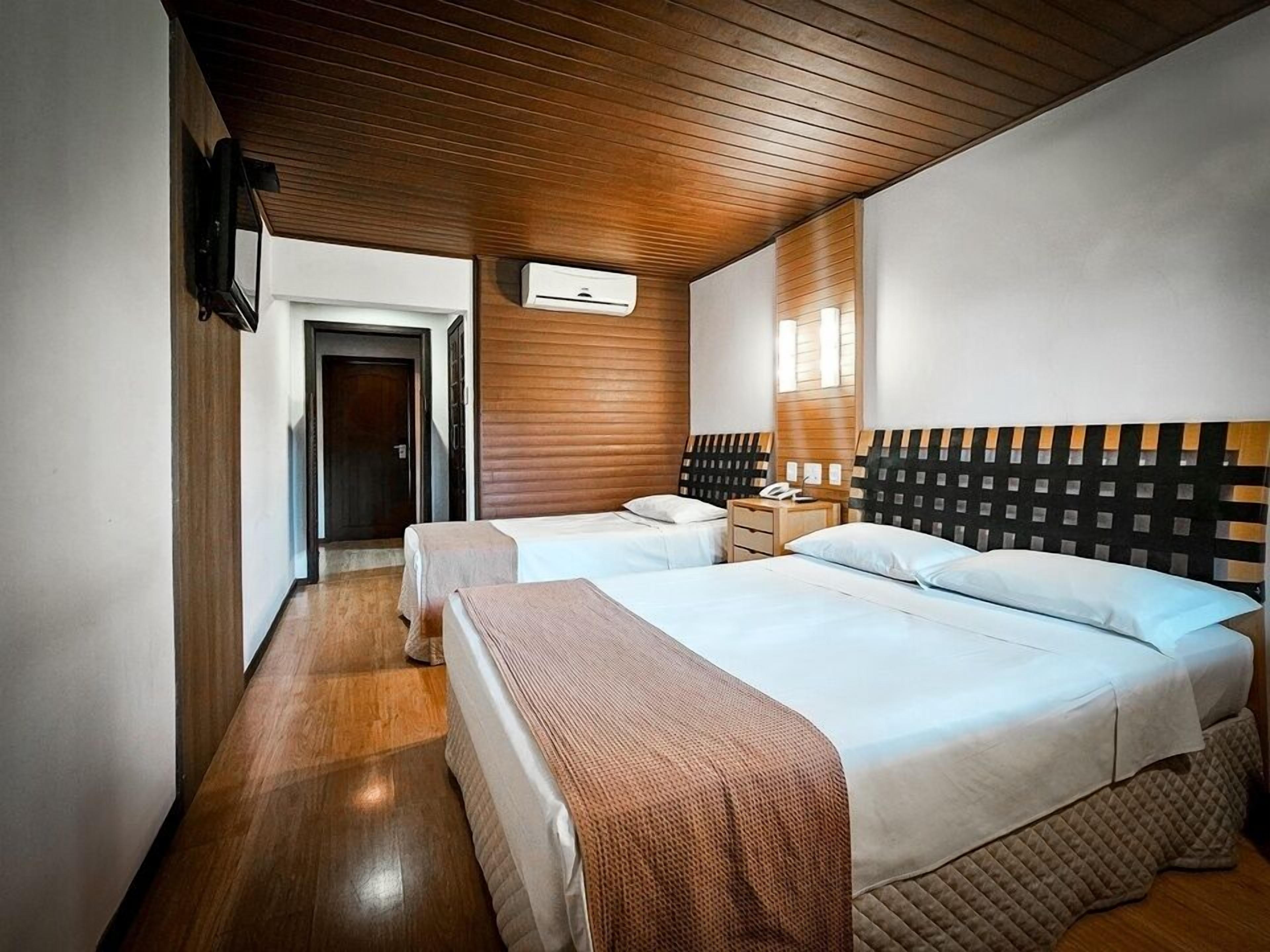 A hotel room with two beds, wooden ceiling, and a nightstand with a phone.