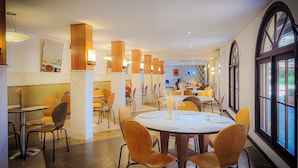 Een moderne eetruimte met ronde tafels en oranje stoelen, houten details en een groot raam met uitzicht op de omgeving.