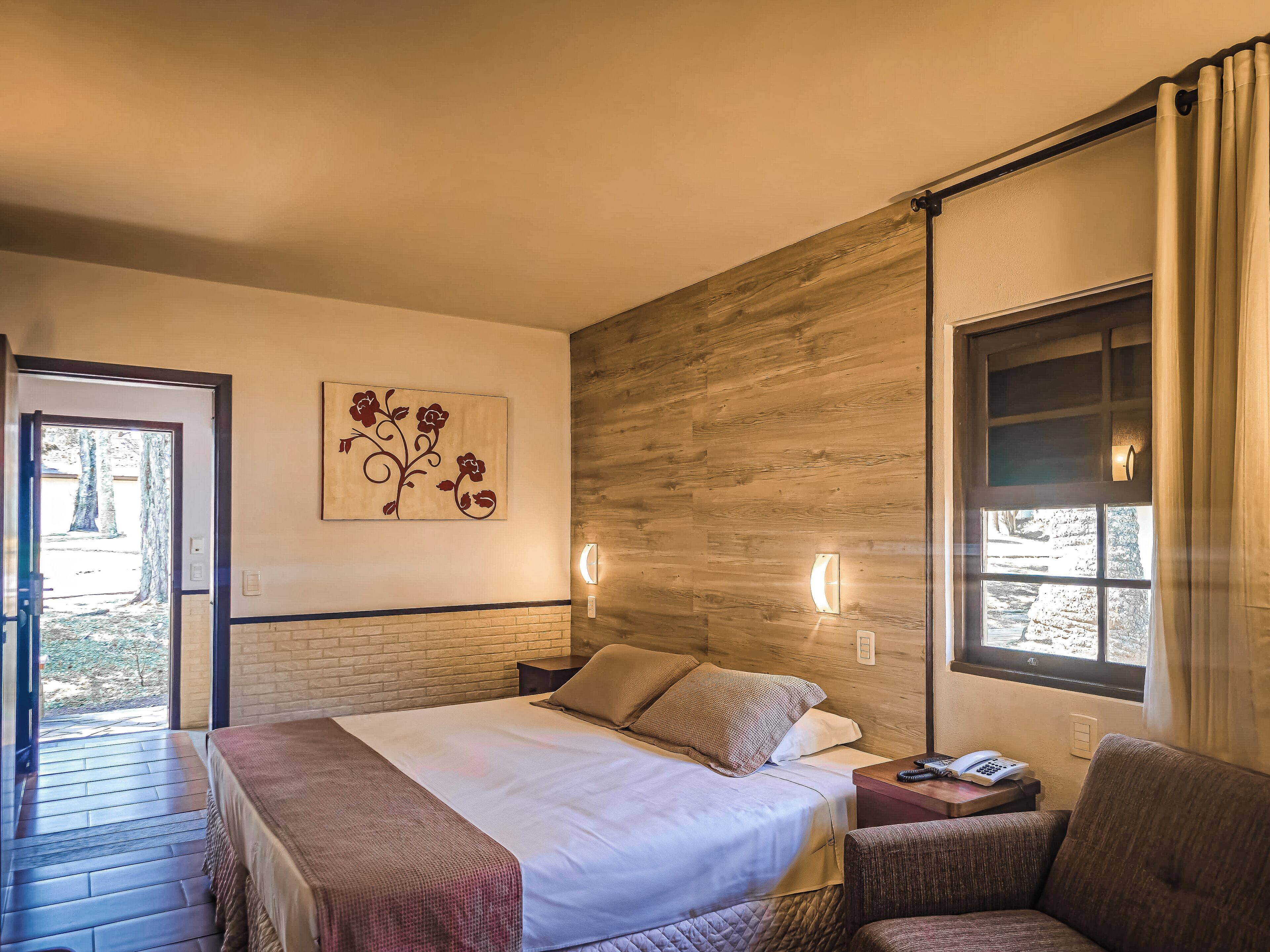 A hotel room with a bed, a chair, a nightstand, and a window with curtains.