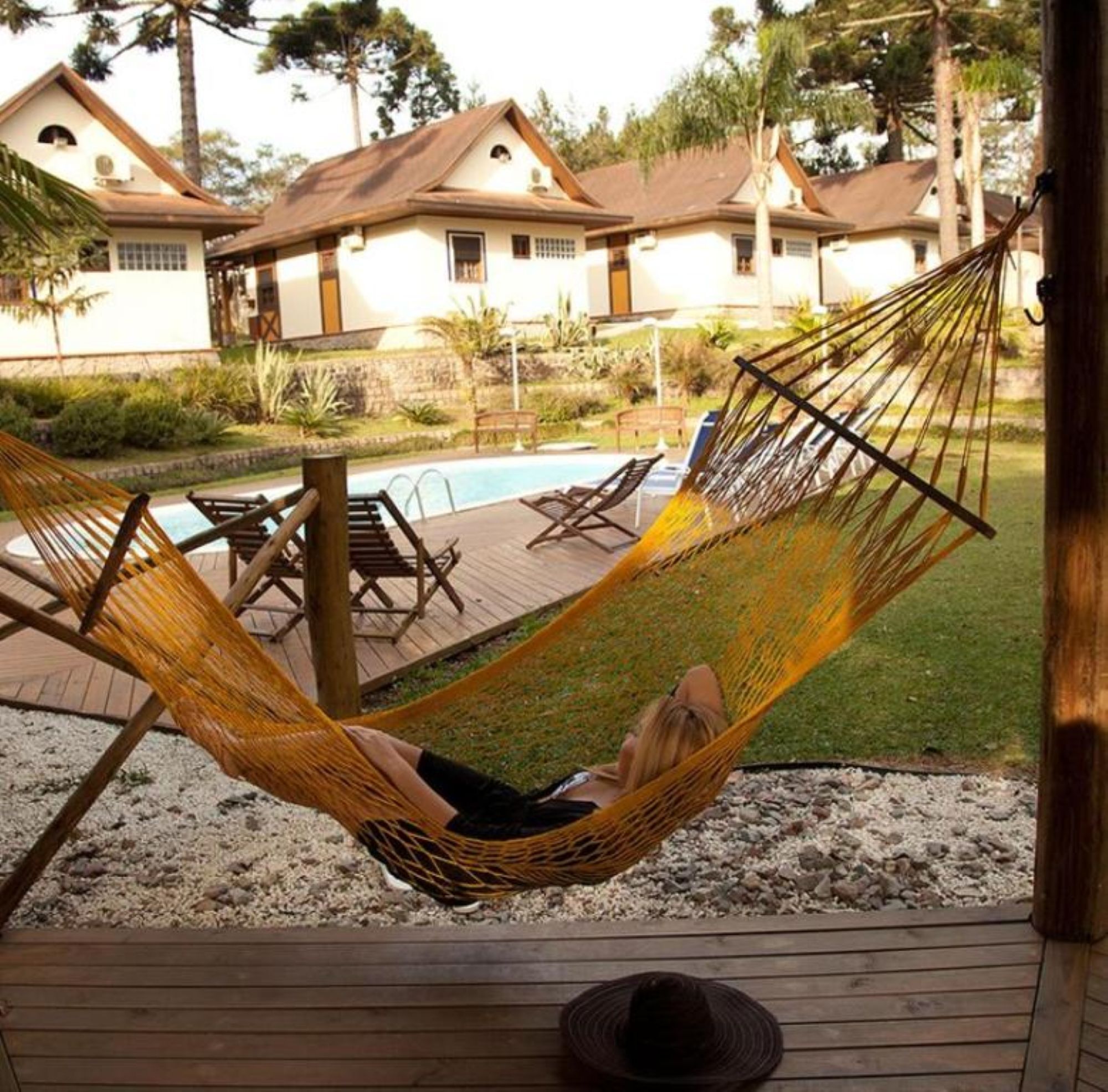 A hammock on a wooden deck with a pool and lounge chairs in the background.