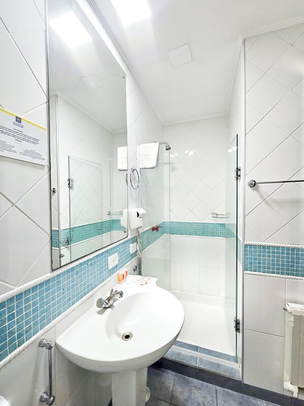 Un baño con lavamanos blanco, cabina de ducha de vidrio y espejo con zócalo de azulejos azules.