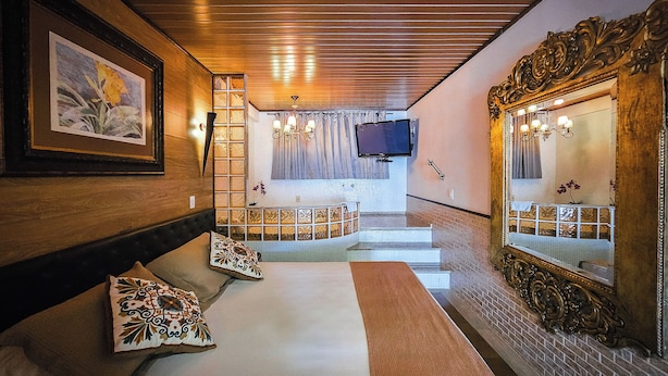 Een hotelkamer met een houten plafond, een grote spiegel, een bed met opvallende kussens, een aan de muur bevestigde televisie en een trap naar een hoger niveau.