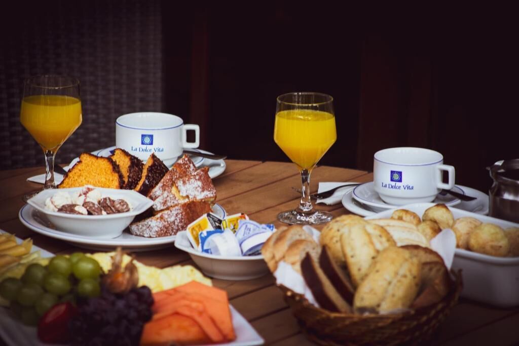 A breakfast table with various food items, including bread, pastries, and fruits, along with two glasses of orange juice.