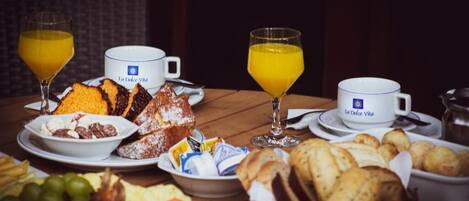 A breakfast table with various food items, including bread, pastries, and fruits, along with two glasses of orange juice.