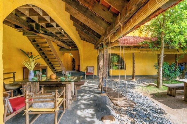 Un espace de restauration extérieur de style rustique, avec une table et des chaises en bois, un escalier et une balançoire suspendue.