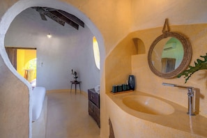 Une salle de bain dotée d’un plafond voûté original, d’un miroir rond et d’un lavabo avec une étagère en bois.