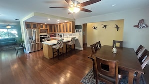 A spacious kitchen with wooden cabinets, a central island with bar stools, a dining table with chairs, and a ceiling fan.
