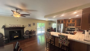 A spacious kitchen with wooden cabinets, a central island with bar stools, a built-in stove, and a ceiling fan.