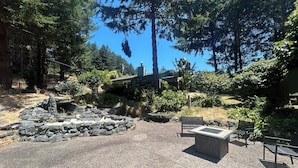 A stone patio with a fire pit, seating area, and surrounding greenery.