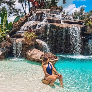 A woman sitting in a clear pool with a waterfall in the background.