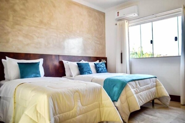 A hotel room with two beds, a large window, and a wall-mounted air conditioner.