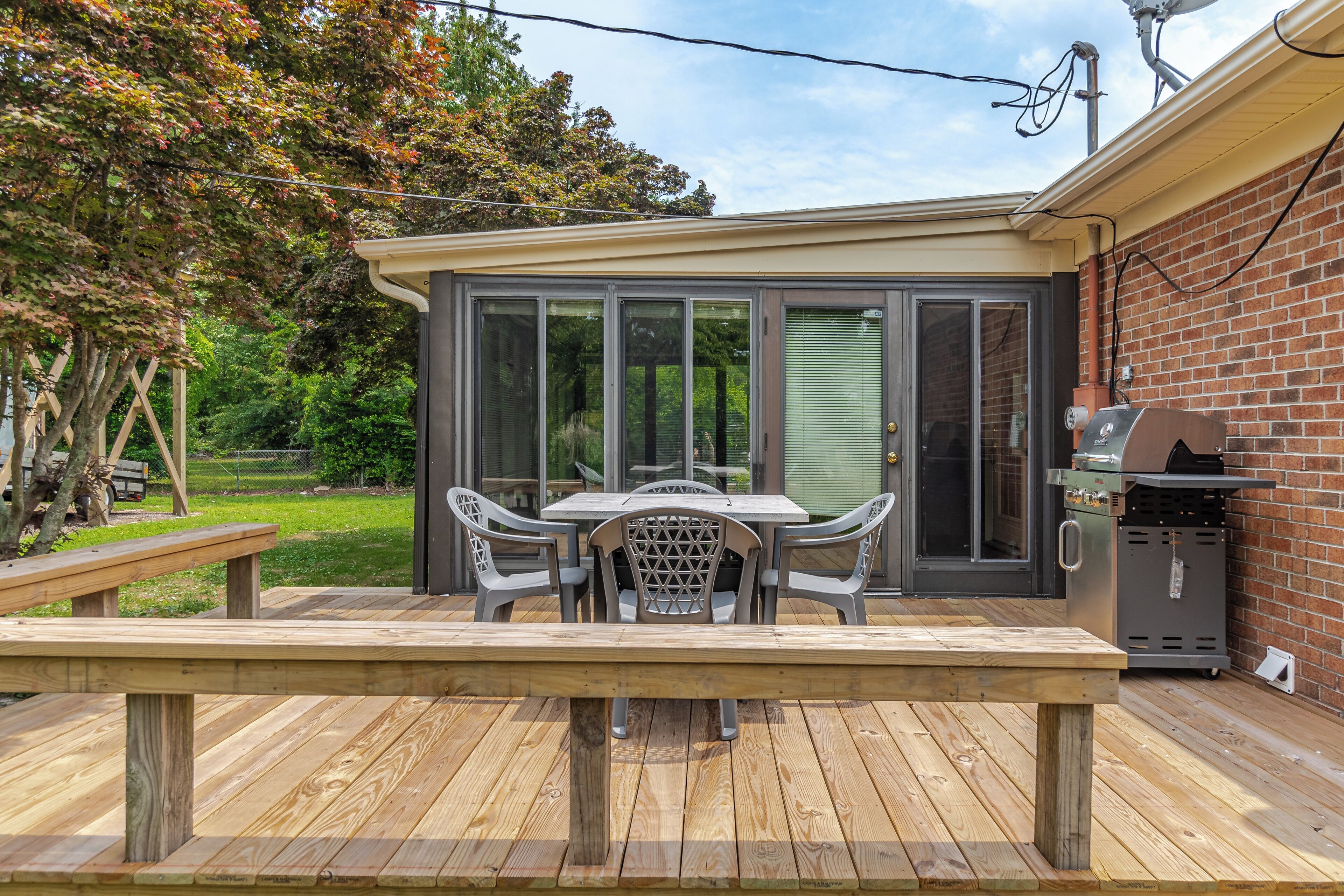 A patio with a wooden table and chairs, a grill, and a sliding glass door leading to a covered area.