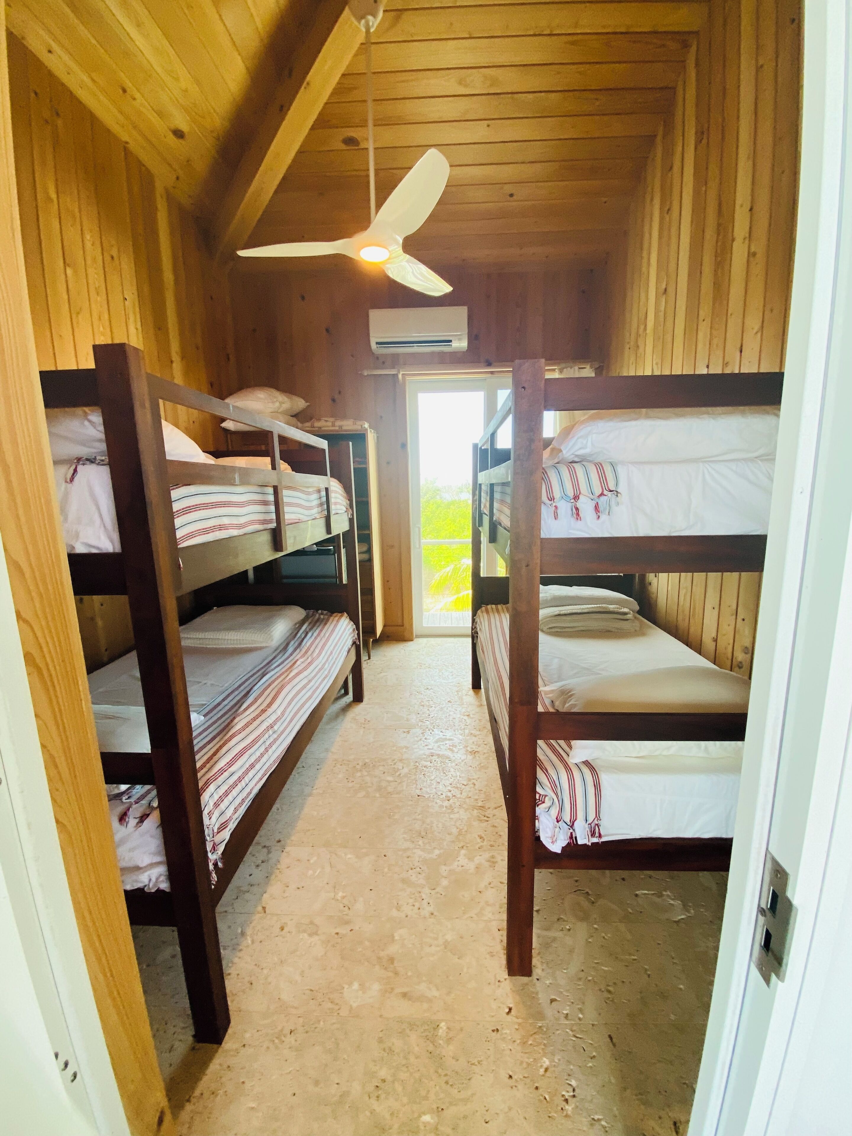 A wooden cabin with bunk beds, a ceiling fan, and a door leading outside.
