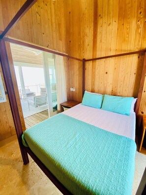 A wooden four-poster bed with a green and white bedspread in a room with wooden walls and a glass door leading to an outdoor area. - Cayo Costa, Pearl of the Island (Captiva)
