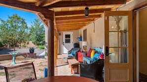 Ein überdachter Patio-Bereich mit Gartenmöbeln, einer Holzbalkendecke und einer Tür zum Innenbereich.