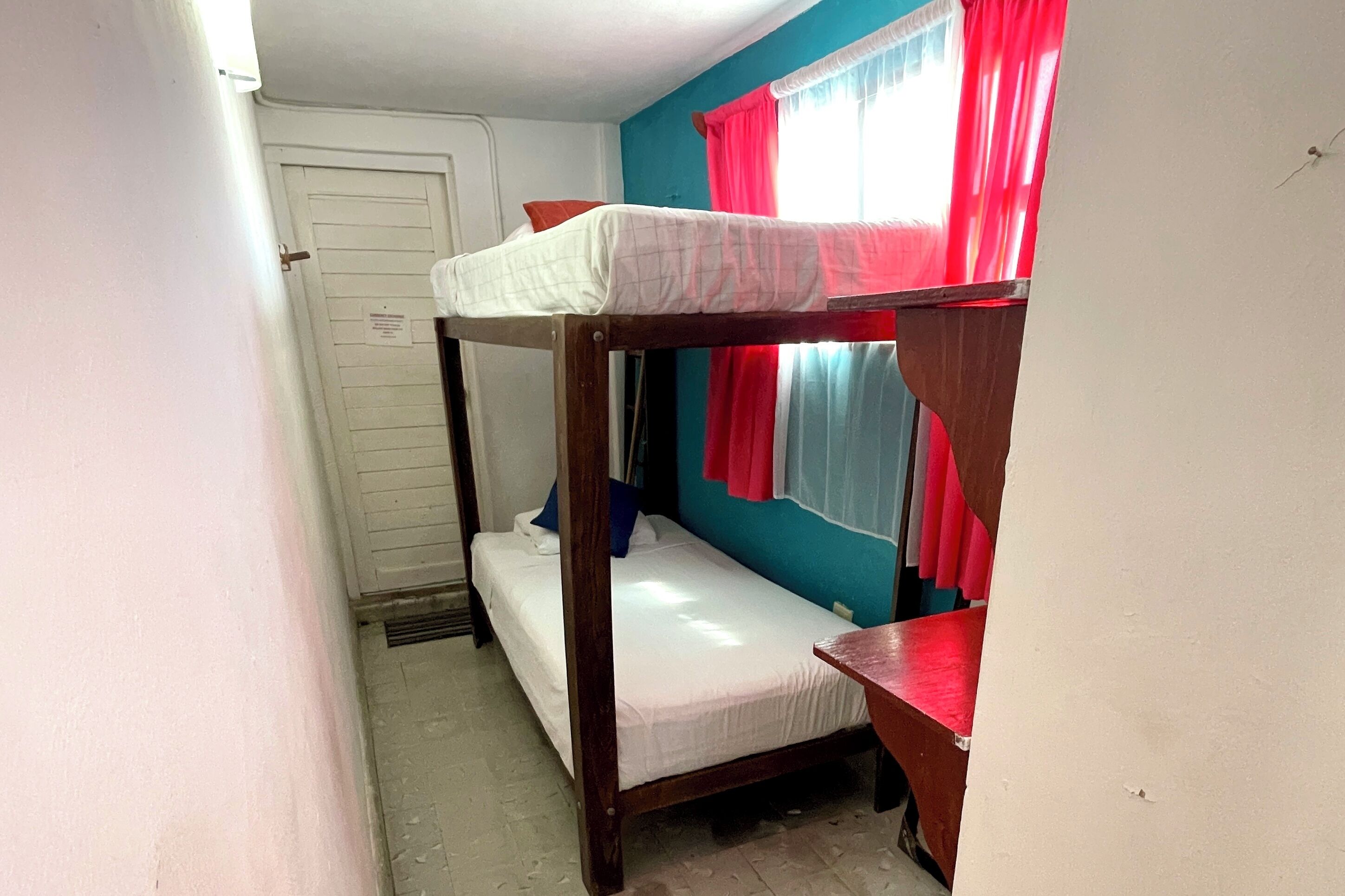 Habitación con literas, ventana, puerta y una mesita pequeña.