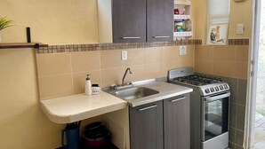 Een kleine keuken met een spoelbak, fornuis en keukenkastjes.