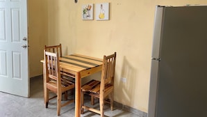 Een eetruimte met een houten tafel en stoelen, een koelkast, en twee wanddecoraties.