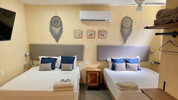Een kamer met twee bedden, een plafondventilator, een airconditioner en decoratieve wandversieringen.