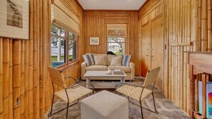 A room with bamboo paneling, a beige sofa, two wicker chairs, a coffee table, and a bookshelf. - Horsepen Cottage on the Water !!!! (Tybee Island)