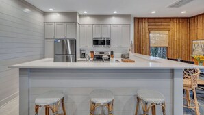 A modern kitchen with white cabinetry, stainless steel appliances, and a central island with bar stools. - Horsepen Cottage on the Water !!!! (Tybee Island)