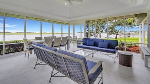 A covered outdoor seating area with a view of the water, featuring wicker chairs, a blue sofa, and a ceiling fan. - Horsepen Cottage on the Water !!!! (Tybee Island)